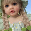 A close-up of a blonde toddler doll with long braided hair wearing a light green dress and a matching bonnet.