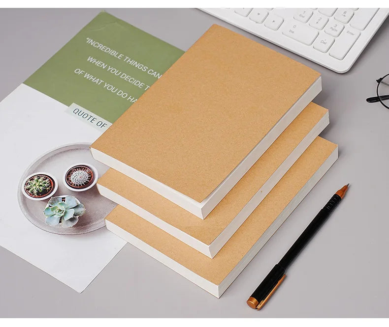 A stack of kraft paper notebooks and a pen on a desk with a quote card.