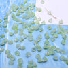 A pile of light green glass beads shaped like lily of the valley flowers on a white card.