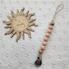 A wooden sun-shaped bead pacifier clip with a silicone teether on a white fabric background.