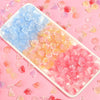 A rectangular dish filled with pink and clear glass beads for jewelry making, scattered on a pink background.