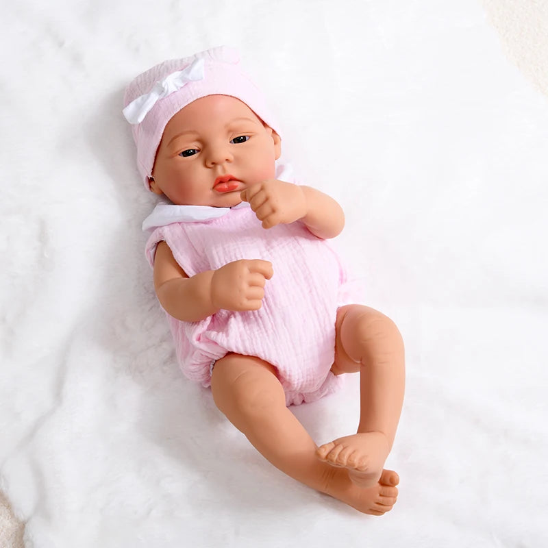 A lifelike vinyl reborn doll with a pink outfit and matching bonnet lying on a white surface.