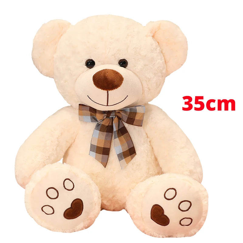 A fluffy, light beige teddy bear plush toy with brown nose and paw pads, tied with a checkered bow.