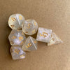 A set of seven glitter gold polyhedral dice, including a d10 and a d20, resting on a brown surface.