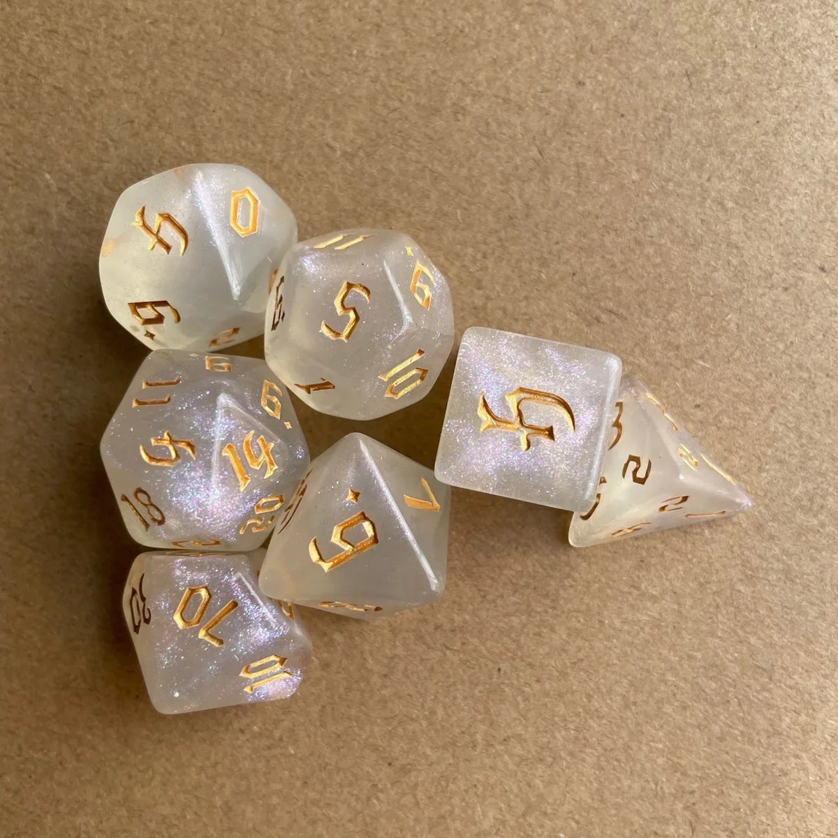 A set of seven glitter gold polyhedral dice, including a d10 and a d20, resting on a brown surface.