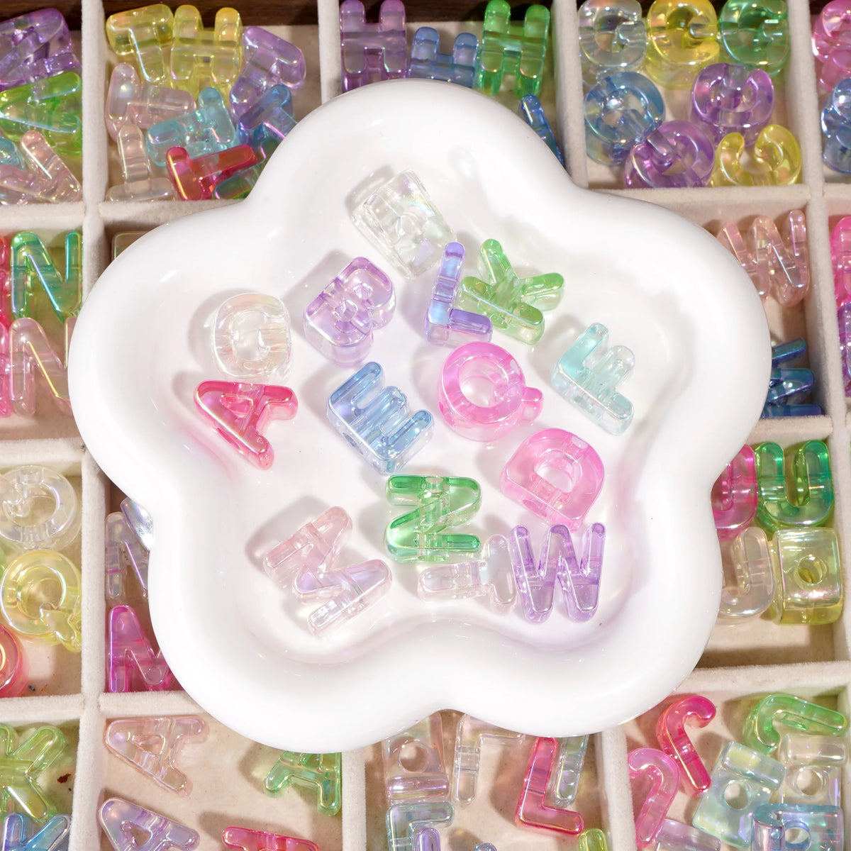 A white mold-shaped tray filled with colorful acrylic alphabet beads for jewelry making and crafts.