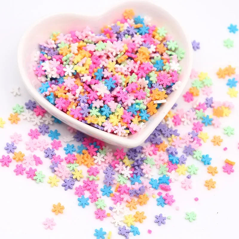 A heart-shaped bowl filled with colorful polymer clay sprinkles for slime decor and DIY craft accents scattered on a white su