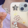 A hand holds a decorative phone charm hook with an adhesive backing next to a smartphone featuring a clear case and a floral 