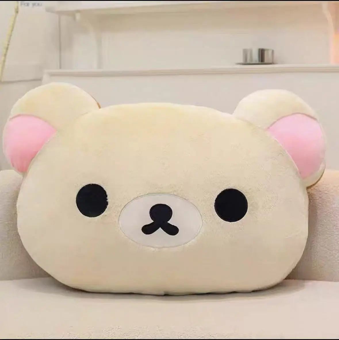 A soft, cream-colored Rilakkuma plush hand rest pillow with pink ears and black facial features.