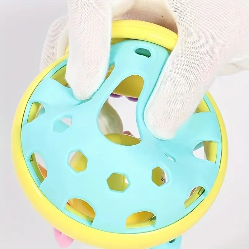 A hand is holding a light blue sensory catch ball rattle toy with yellow accents.