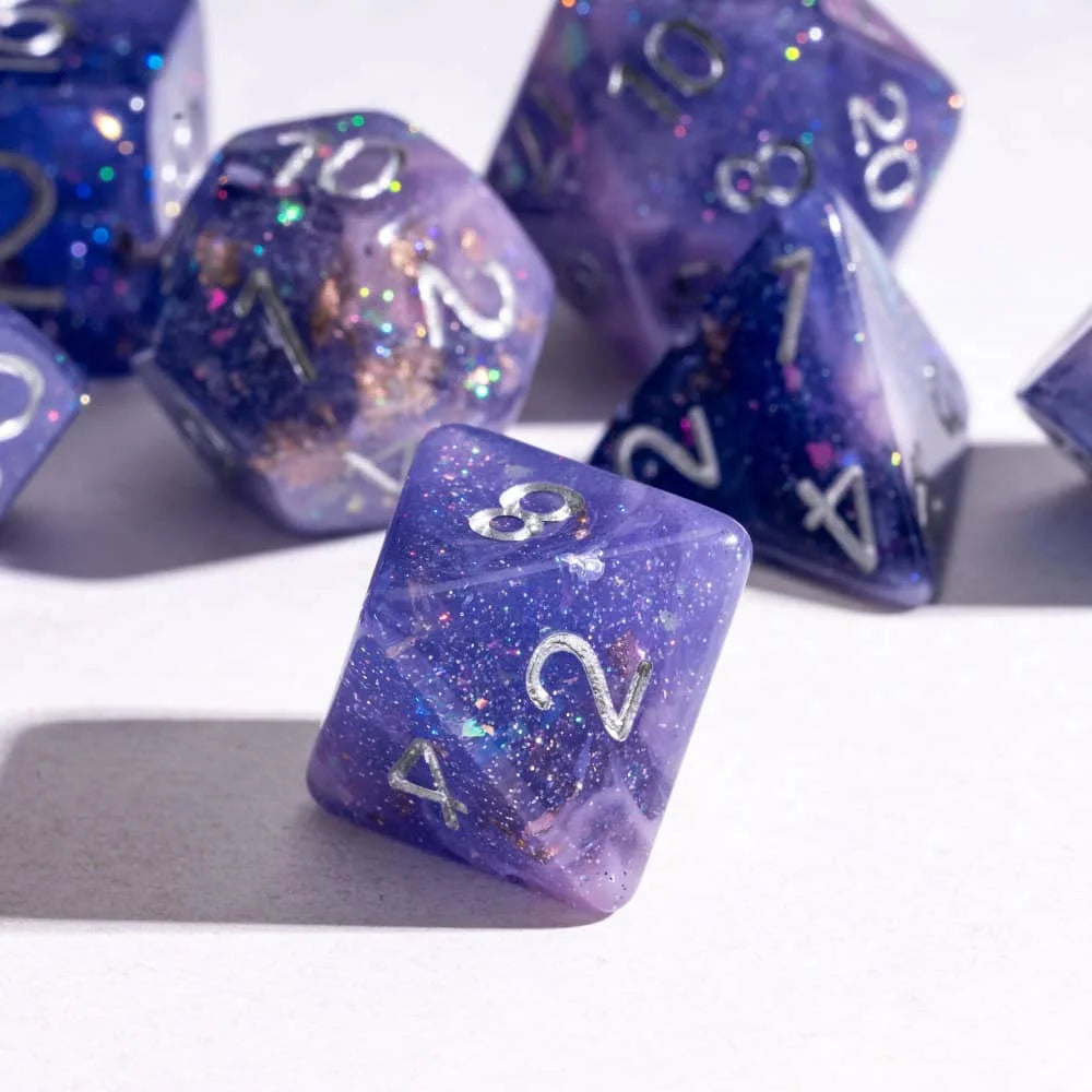 A close-up of several purple glitter resin polyhedral dice scattered on a white surface.