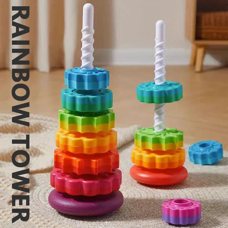 A stack of colorful rainbow spinning rings and a white tower for toddlers on a light fabric surface.