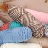 A pile of three skeins of soft cotton blend yarn in various shades including beige, pink, teal, and light blue.