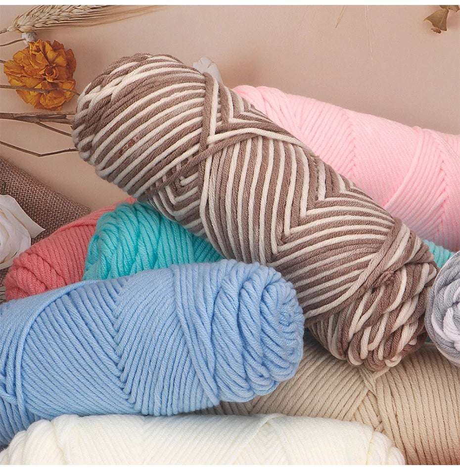 A pile of three skeins of soft cotton blend yarn in various shades including beige, pink, teal, and light blue.