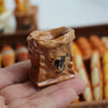 A hand holds a small, brown miniature dollhouse baguette basket set.
