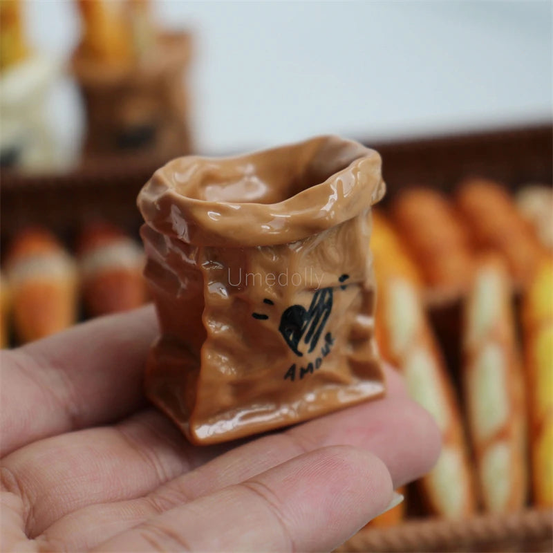 A hand holds a small, brown miniature dollhouse baguette basket set.