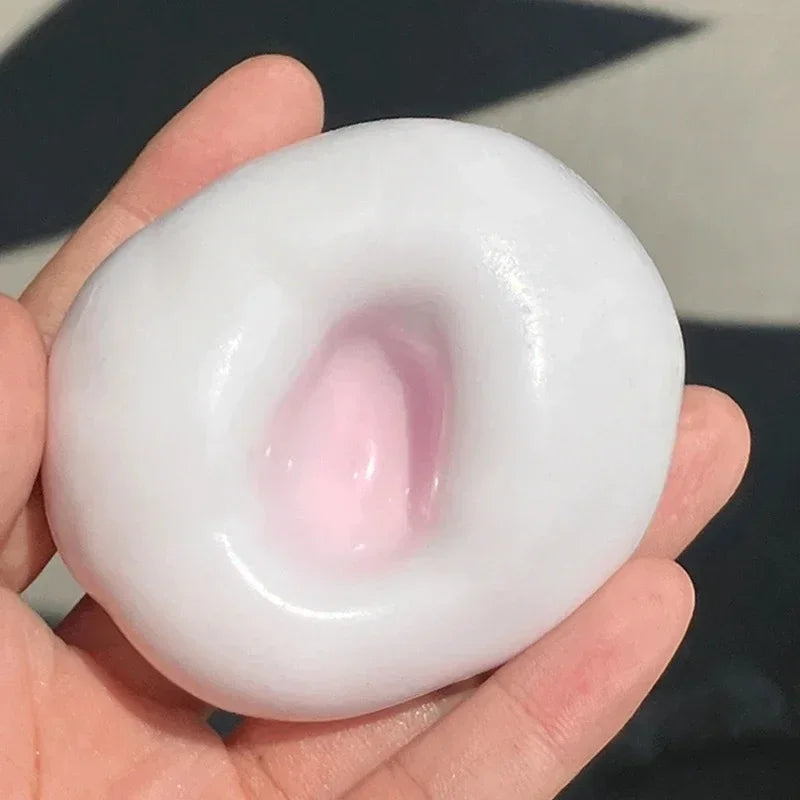 A hand holds a white, squishy stress relief ball with a pink center, demonstrating its texture.