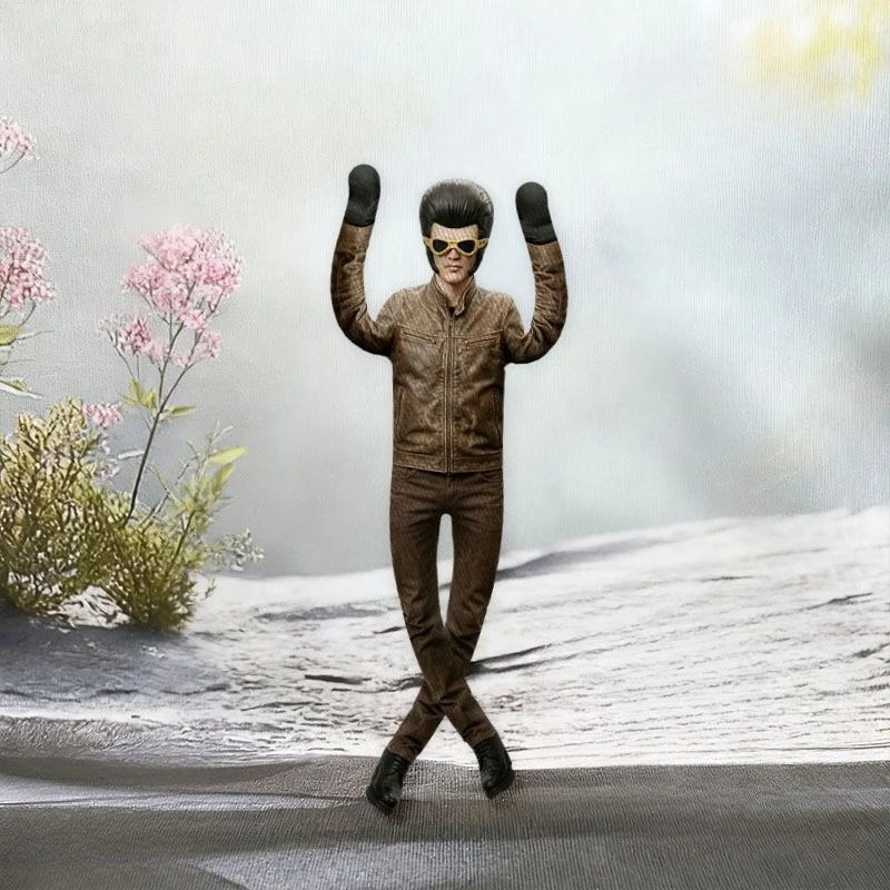 A collectible plush doll of Elvis Presley in a brown leather jacket and sunglasses posing with his arms raised against a snow