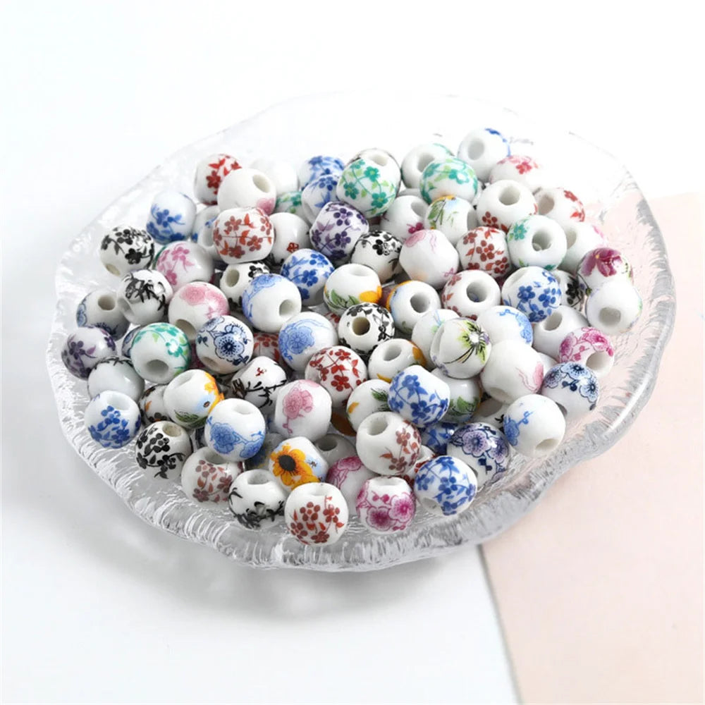 A set of 20 round ceramic flower beads in various colors and patterns, including white, blue, pink, and green, displayed in a