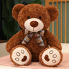 A brown teddy bear plush pillow with a plaid bow and embroidered features.