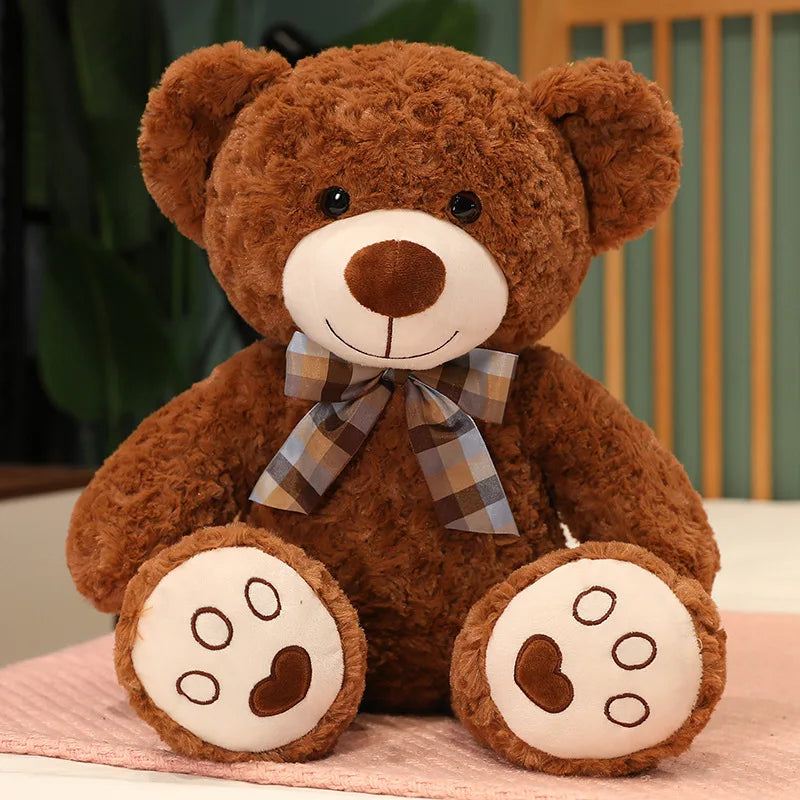 A brown teddy bear plush pillow with a plaid bow and embroidered features.