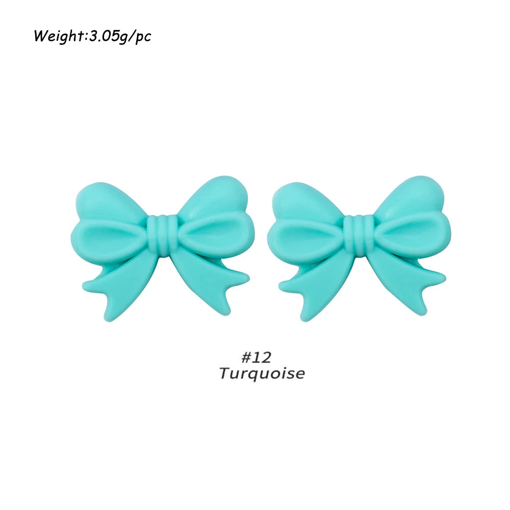 A pair of light blue silicone bow tie beads used for jewelry making and craft projects.