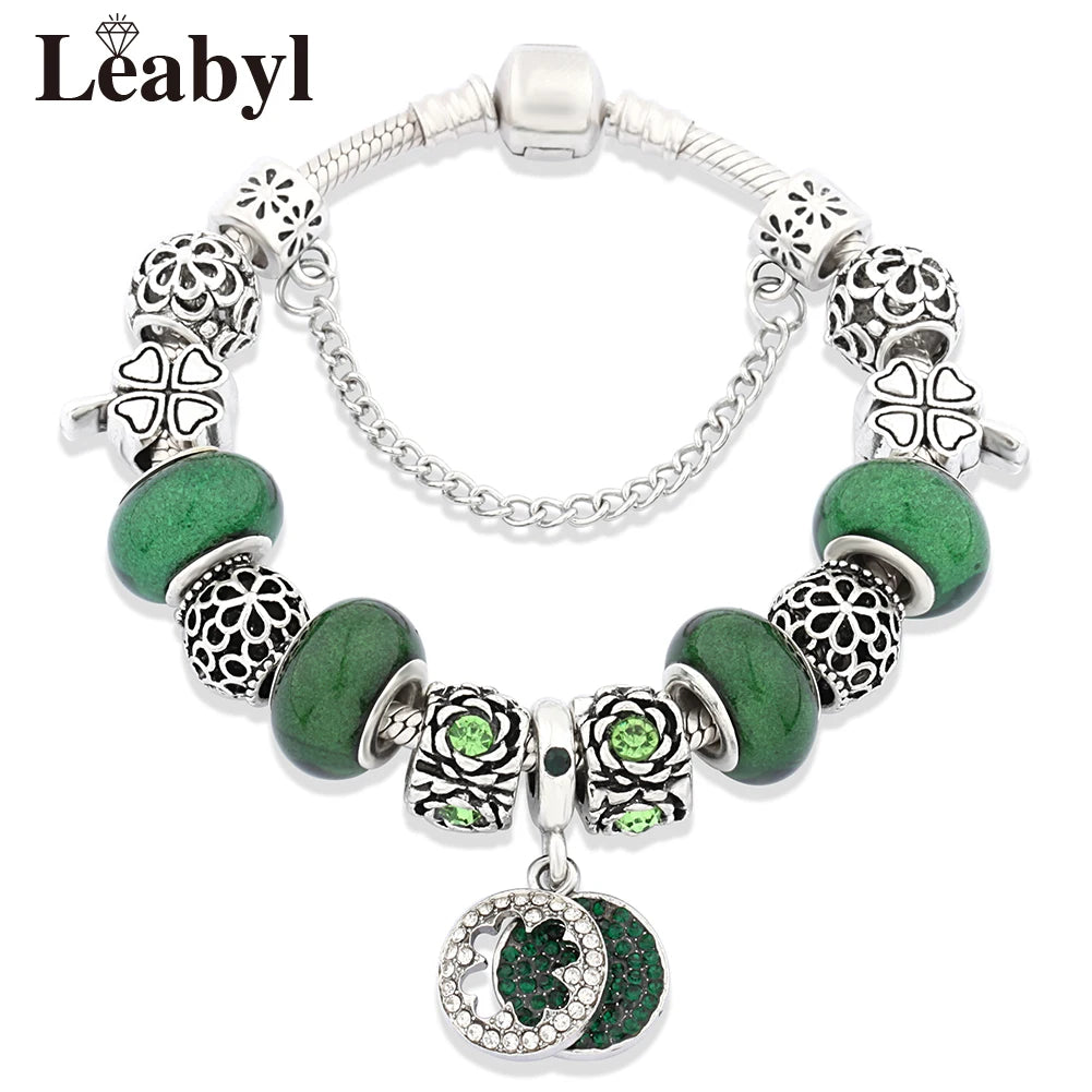 Silver crystal charm bracelet featuring green leaf and floral accents with intricate metalwork.