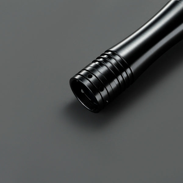 Primer plano de la empuñadura de un sable de luz Neopixel negro sobre una superficie gris oscuro.