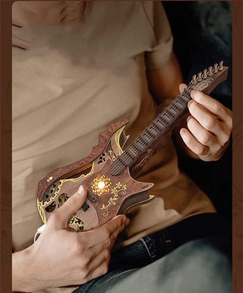 A person holds a wooden miniature guitar model kit, showing the detailed buildable puzzle craft for music lovers.