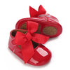 A pair of red lace-trimmed baby girl moccasin shoes with large red bows.