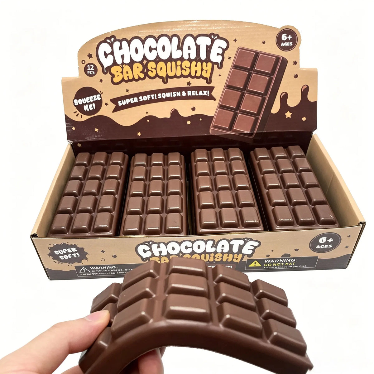 A box of chocolate bar squishy toys is shown with several brown squishy blocks and a single squishy toy being held by a hand.