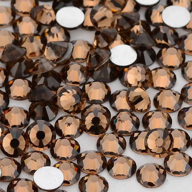 A close-up view of small, round, amber-colored glass crystal flatback rhinestones for nail art and crafts.
