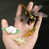 A hand holds a set of insects and a flower, including a dragonfly, a wasp, and a caterpillar, for learning.