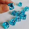 A hand holds a set of bright blue transparent dice with white polka dots on a white surface.