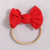 A bright red fabric bow headband with a light beige elastic band, suitable for a baby or girl.