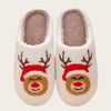 A pair of beige plush indoor slippers with brown reindeer faces and red hats.