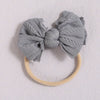 A gray fabric bow headband with a light beige elastic band resting on a white surface.