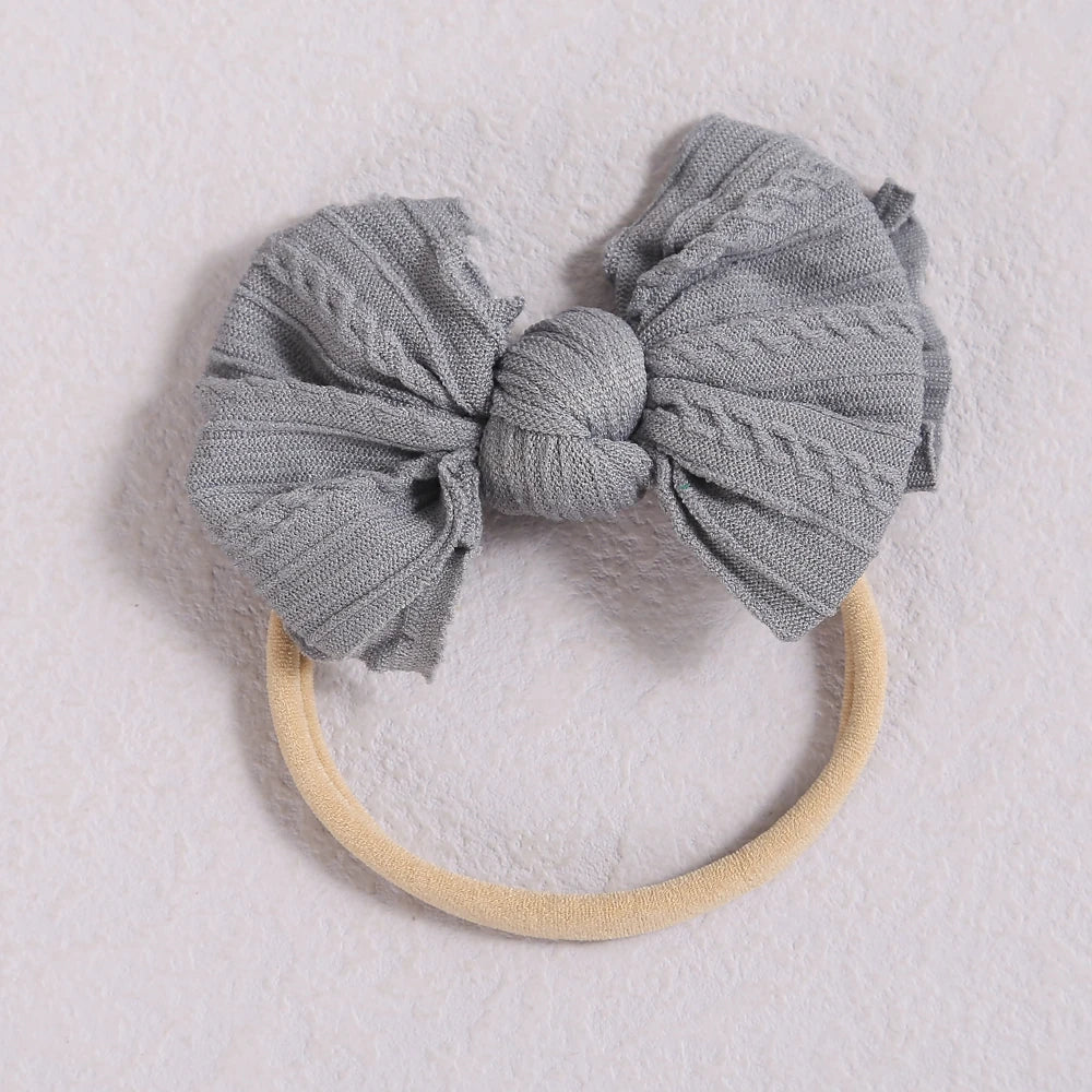 A gray fabric bow headband with a light beige elastic band resting on a white surface.