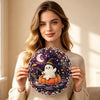 A woman holds a Halloween diamond painting ornament kit featuring a white ghost and a crescent moon on a dark purple backgrou