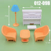 A dollhouse furniture playset featuring a white piano, an orange chair, and a small table on a green surface.