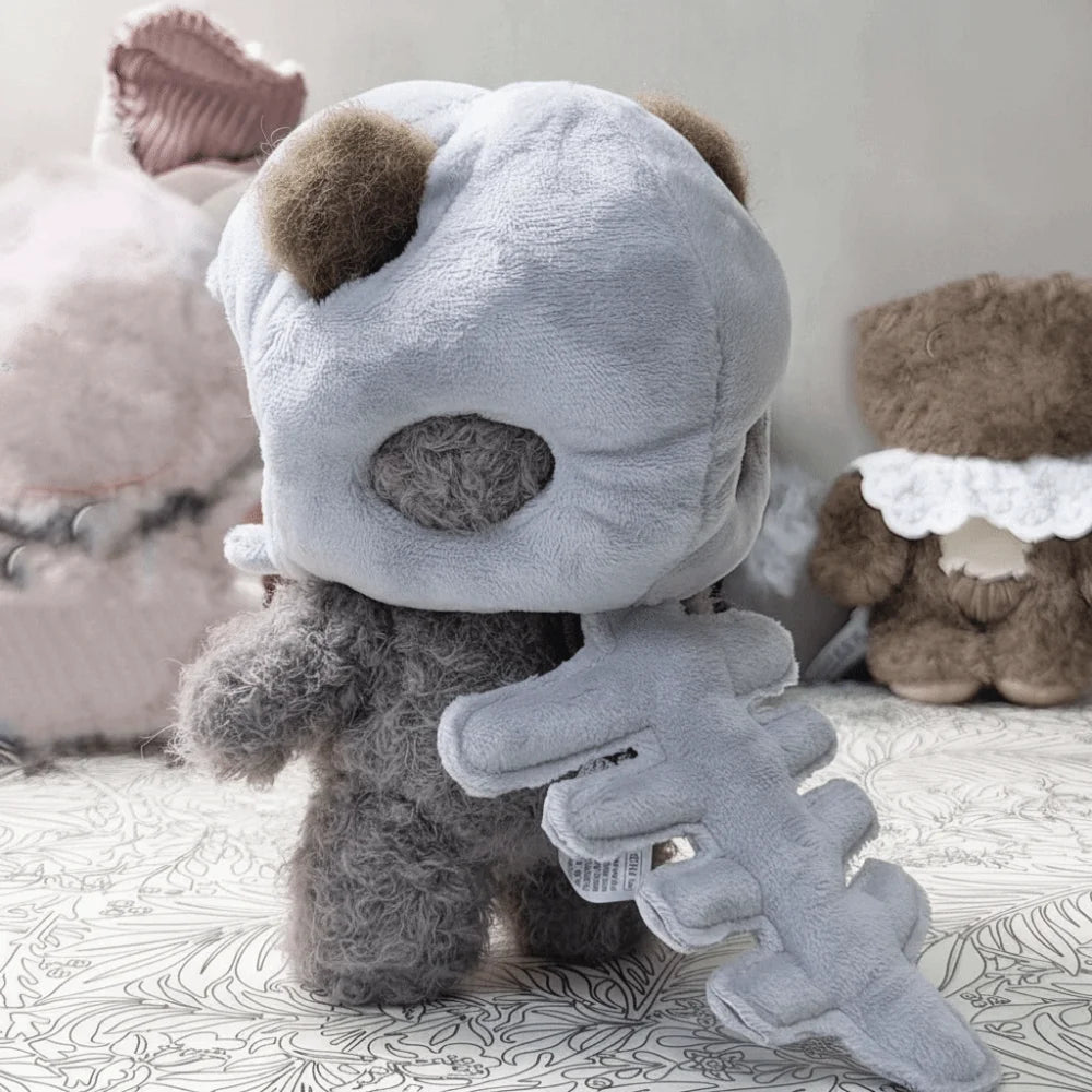A gray dinosaur skeleton bag charm with a removable hood resting on a patterned surface.