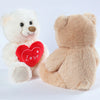 A white plush bear and a tan plush bear with a red heart print on the chest.