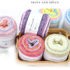 A collection of colorful gradient yarn spools in various shades of purple, pink, and yellow are displayed in a wooden box.