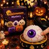 A white squishy dumpling stress relief toy with a purple eye is held above a wooden tray surrounded by Halloween decorations.
