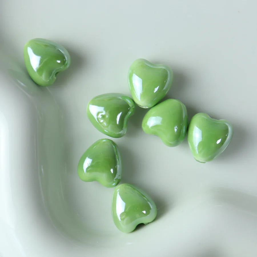 A collection of ten bright green heart-shaped ceramic beads arranged on a light gray surface.