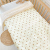 A cream fleece blanket with a subtle pattern is draped over a wooden crib railing.