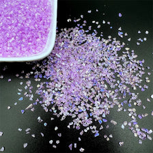 Purple crushed glass crystals scattered on a dark surface next to a white dish.