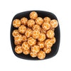 A bowl filled with small, round, orange and white patterned silicone beads for jewelry making.