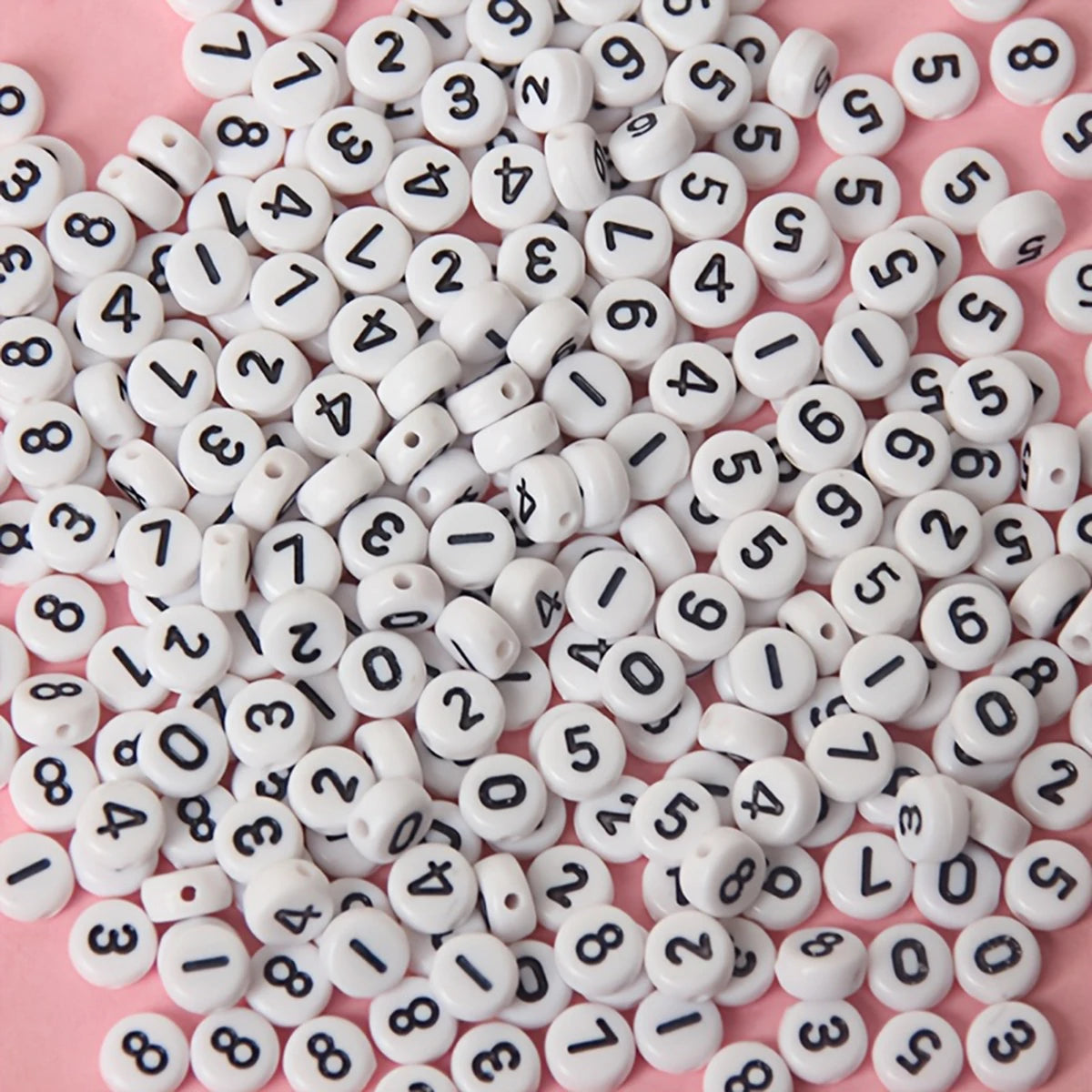 A close-up view of small white acrylic number beads scattered on a pink surface.