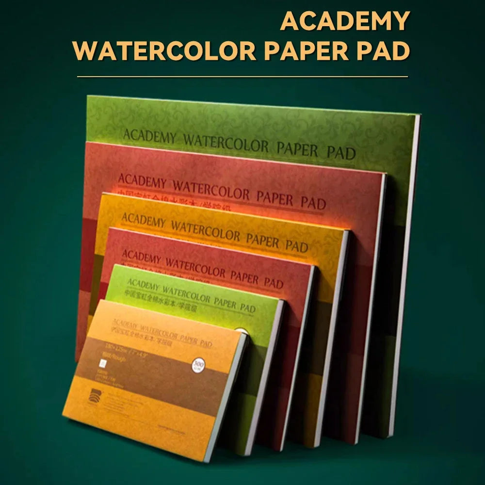A stack of Academy watercolor paper pads in various shades of green, red, and yellow.